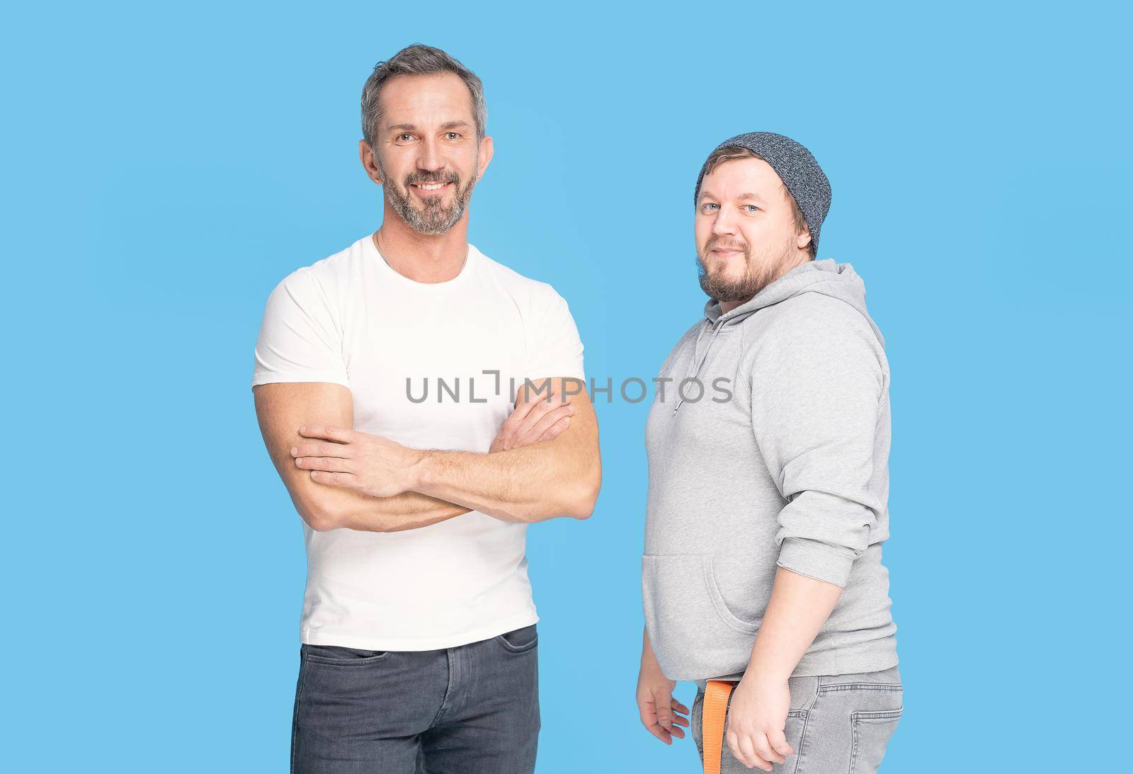 Two types of men. Fat man and fit mature man posing in studio isolated on blue background. Time to get fit trainer man standing next to trainee. Sports concept and man healthcare.