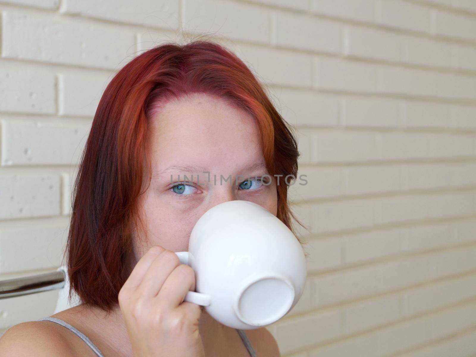 red-haired teenage girl drinks tea from a white cup close-up