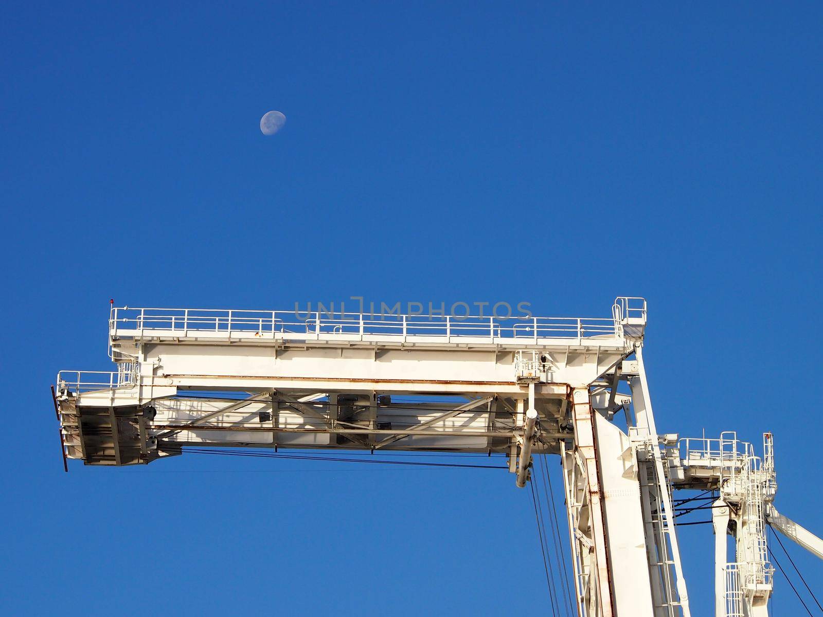 Lifting arm of Large crane with blue sky and half moon in Oakland Harbor, California.