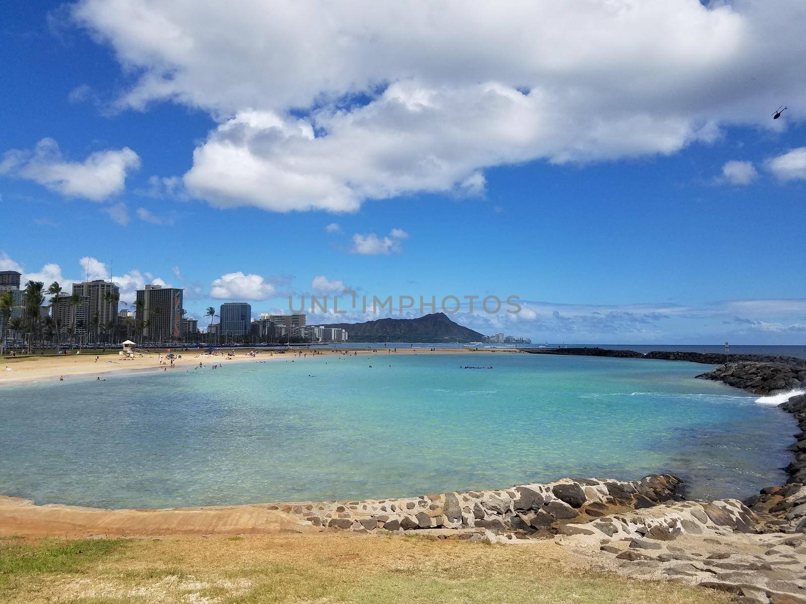 Beach on Magic Island in Ala Moana Beach Park on the island of Oahu, Hawaii.  Waikiki and Diamond Head in the distance and helicopter in the air on a beautiful day.