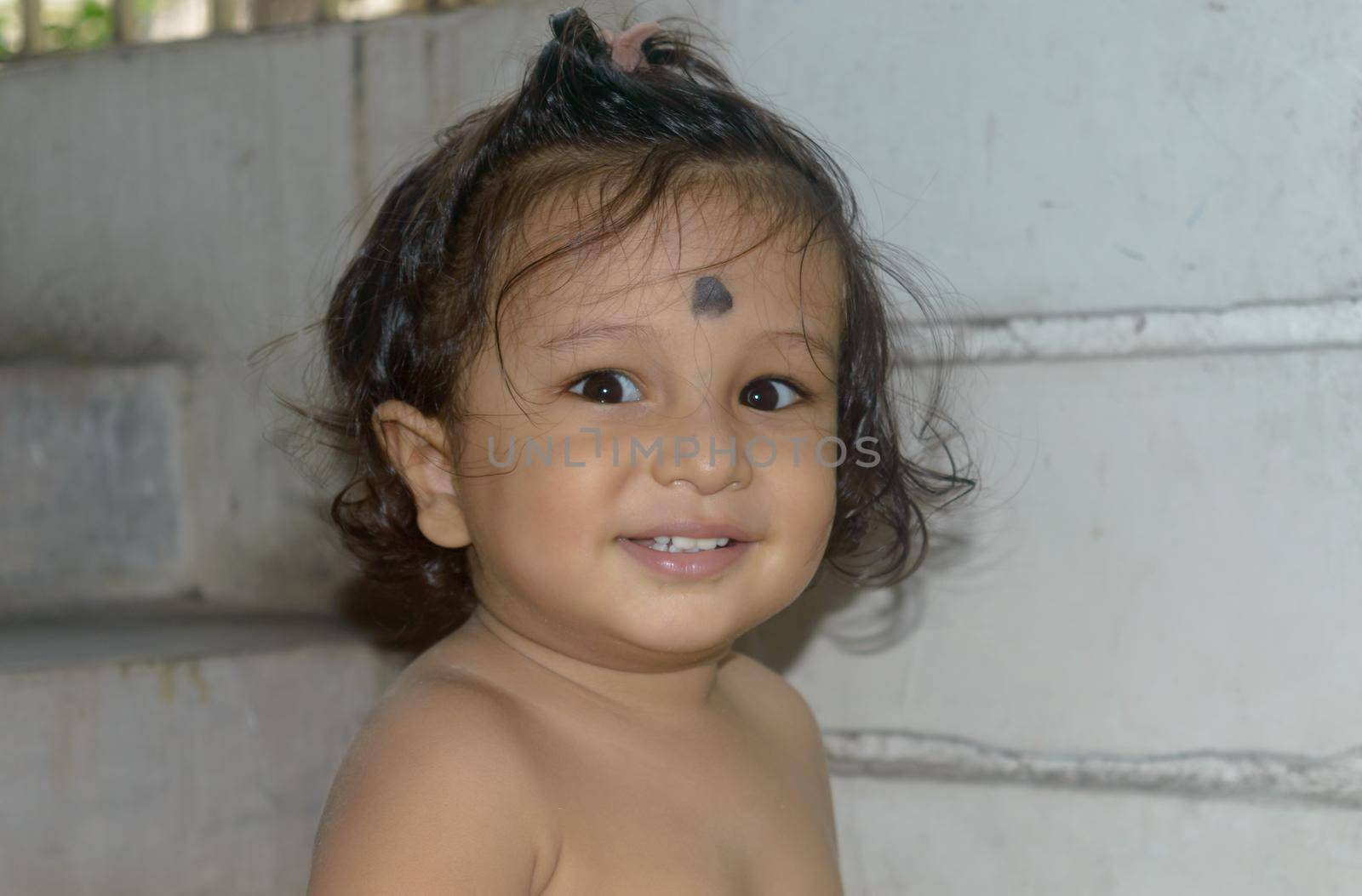 Cute happy indian baby without shirt smiling and looking at camera.