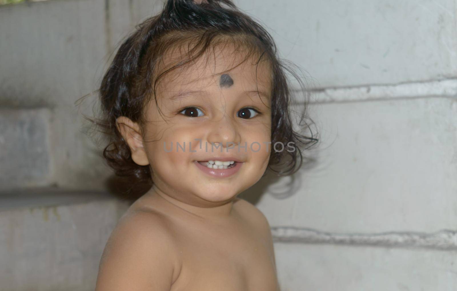 Cute happy indian baby without shirt smiling and looking at camera.