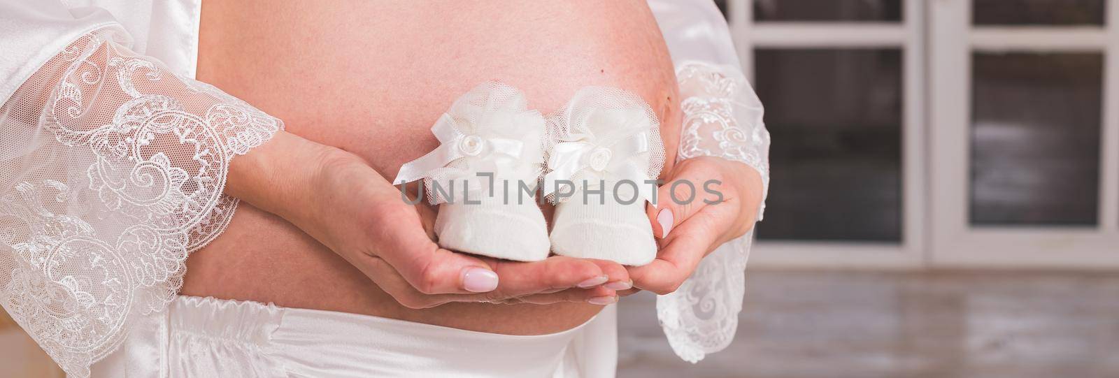 Pregnant woman, belly. Mother hands holding shoes for the newborn baby. Happy girl pregnancy, maternity, body care. Mom Expecting Baby. Baby Shower.Web banner. by YuliaYaspe1979