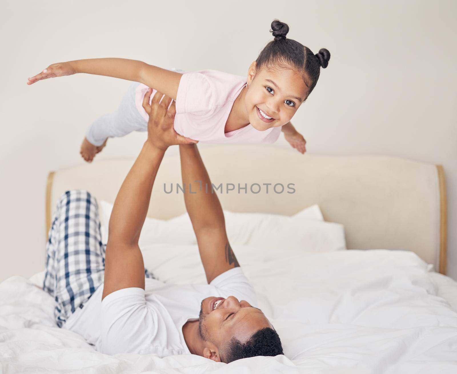 Joyful young father lying on bed, lifting excited happy little child daughter at home. Carefree family having fun in bedroom.