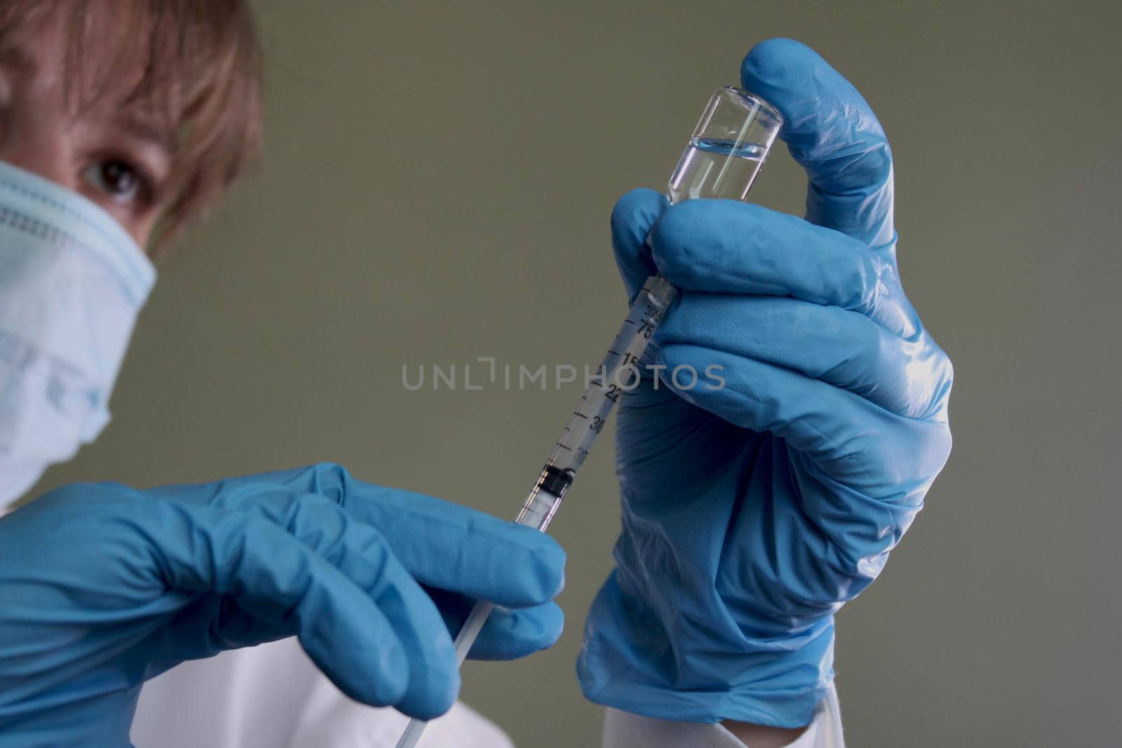 A female doctor in medical gloves and a mask will collect the vaccine from a vial into a syringe..