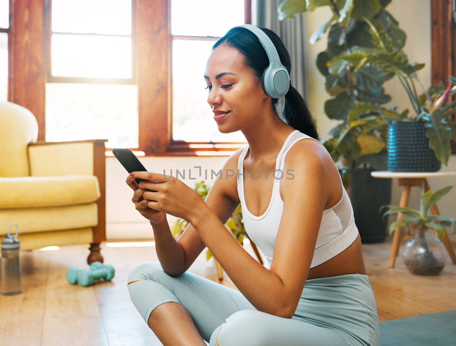 Which songs should I listen to during my session. a sporty young woman wearing headphones and using a cellphone while exercising at home. by YuriArcurs