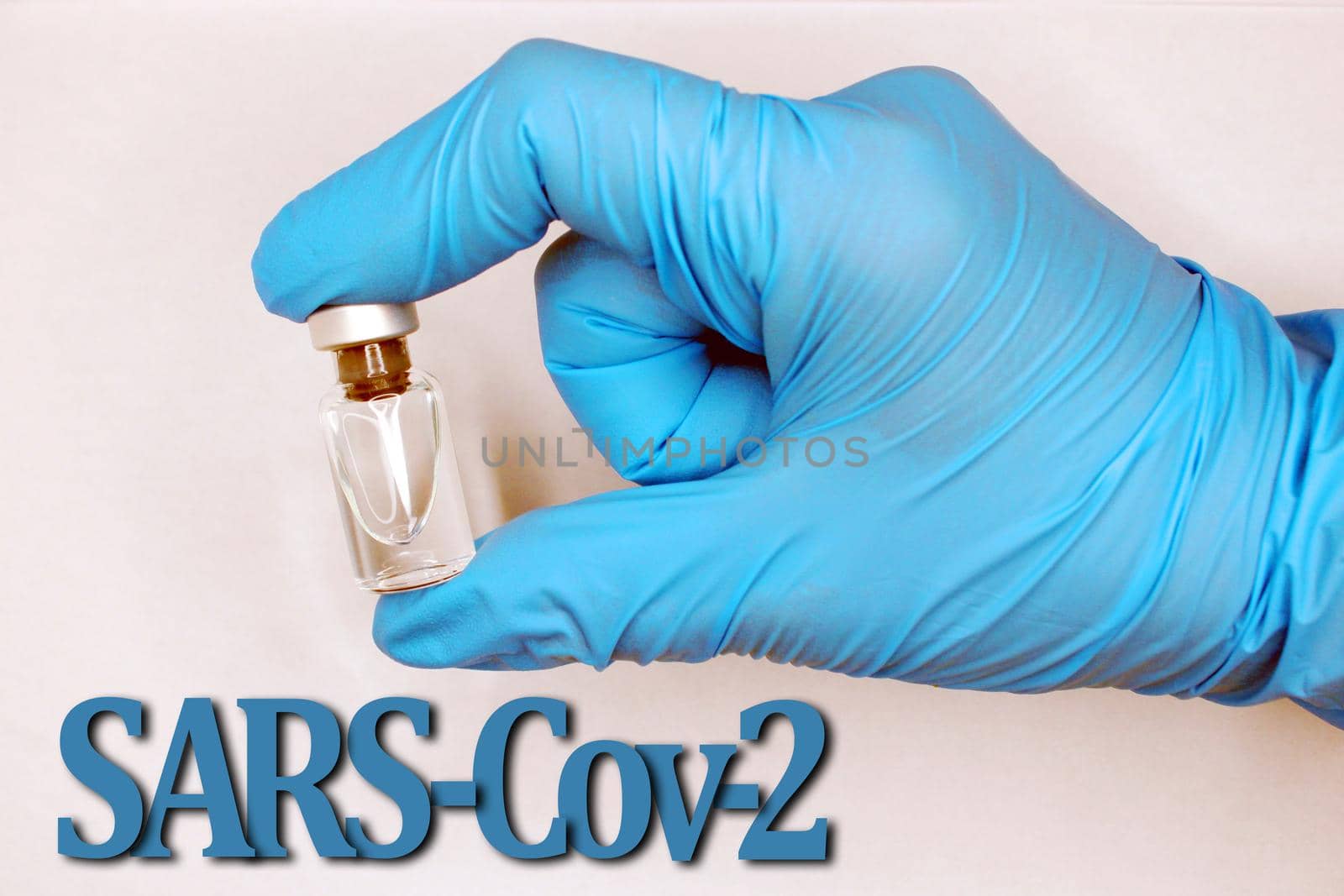 A hand in a blue medical glove close-up with a vaccine. SARS-Cov-2 inscription at the bottom..