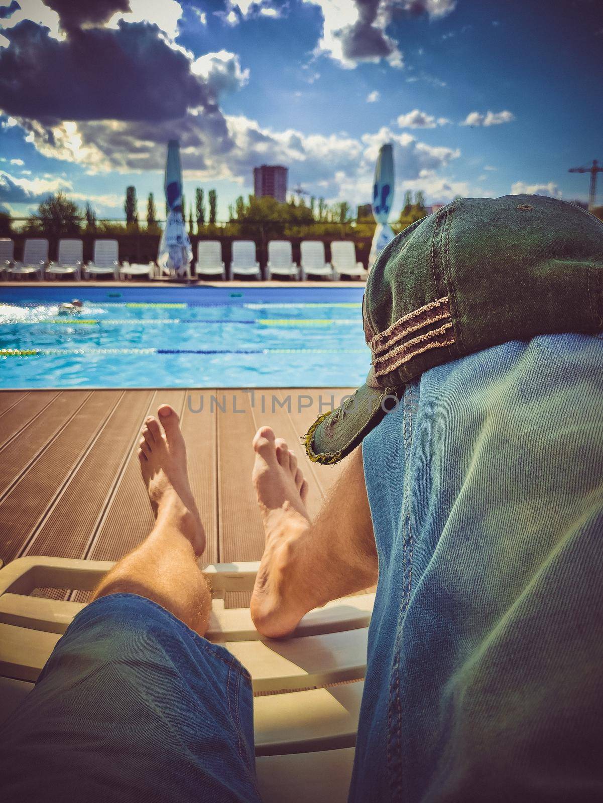 Men's feet on a sun lounger in front of the pool by clusterx