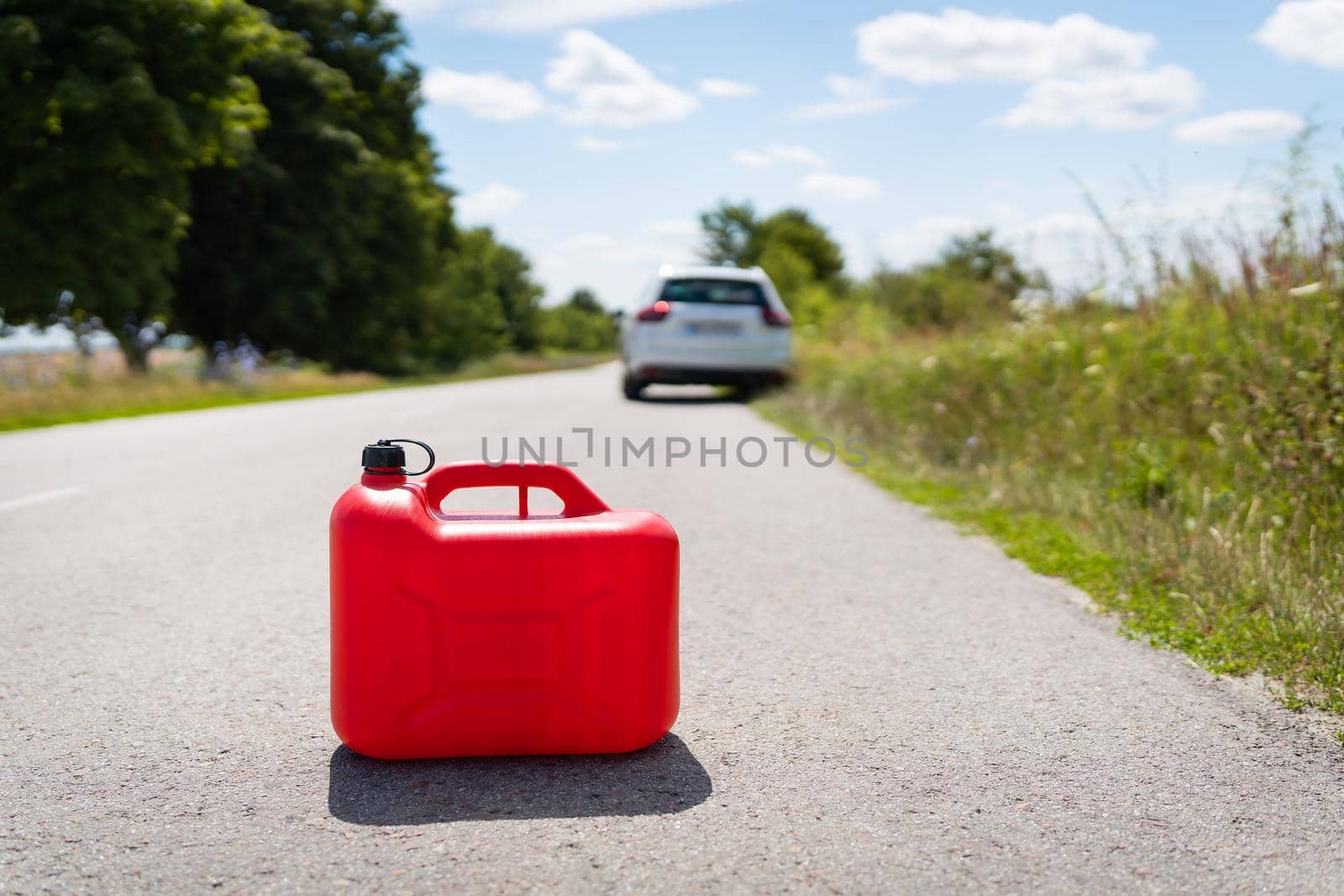 A car parked on the side of the road, an empty red canister. The driver is on the road. Help on the road. Fuel shortage - oil, diesel, gasoline