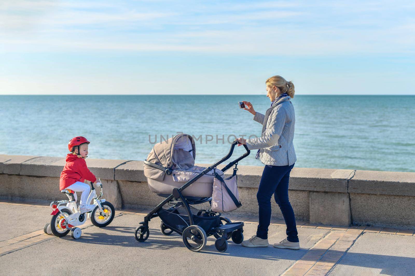 Mother with a stroller and daughter on a bicycle are walking together on the beach by Godi