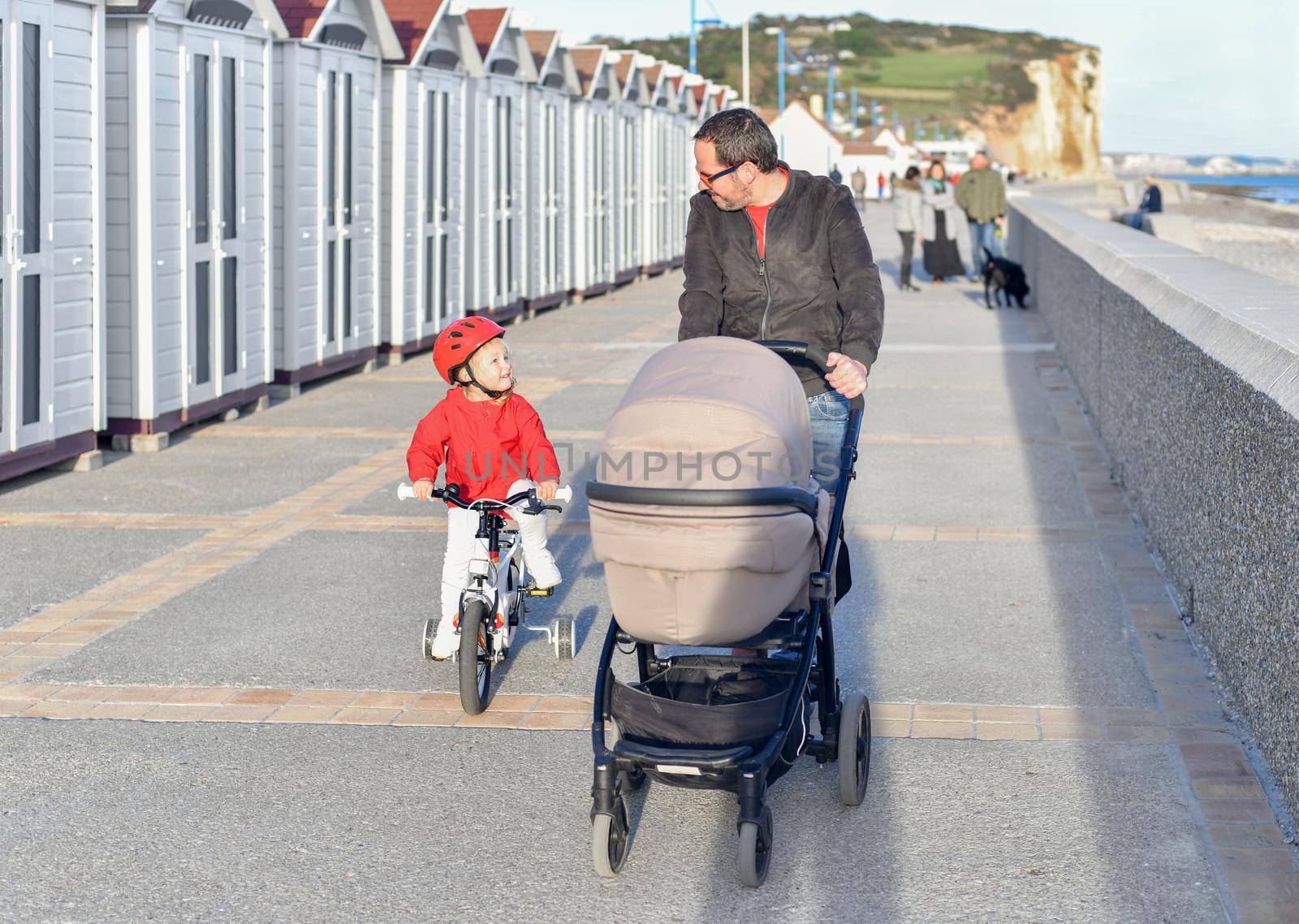 Father with a stroller and daughter on a bicycle are walking together on the beach by Godi