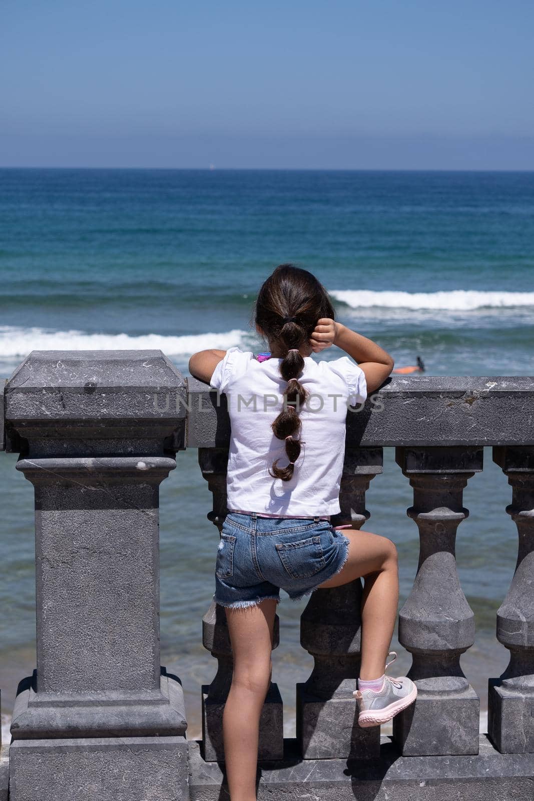 long-haired girl watching surfers in the sea from a vantage point