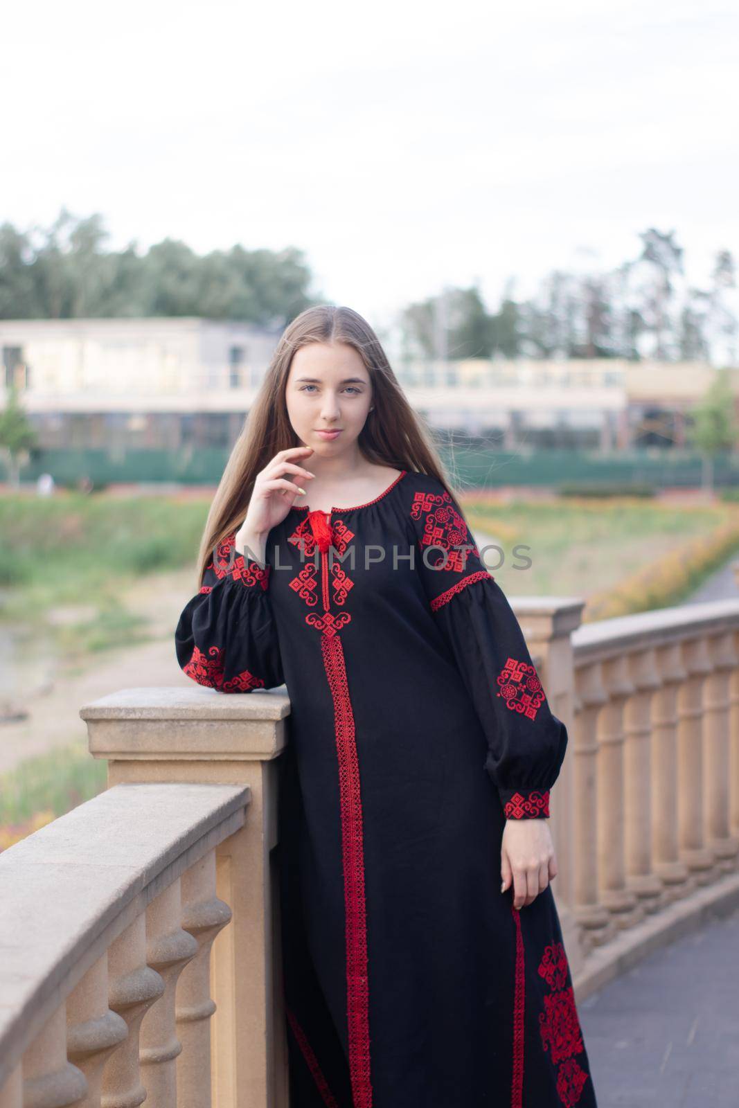 charming ukrainian young woman in embroidered national red and black dress outdoors. pretty girl in park wearing vyshyvanka by oliavesna