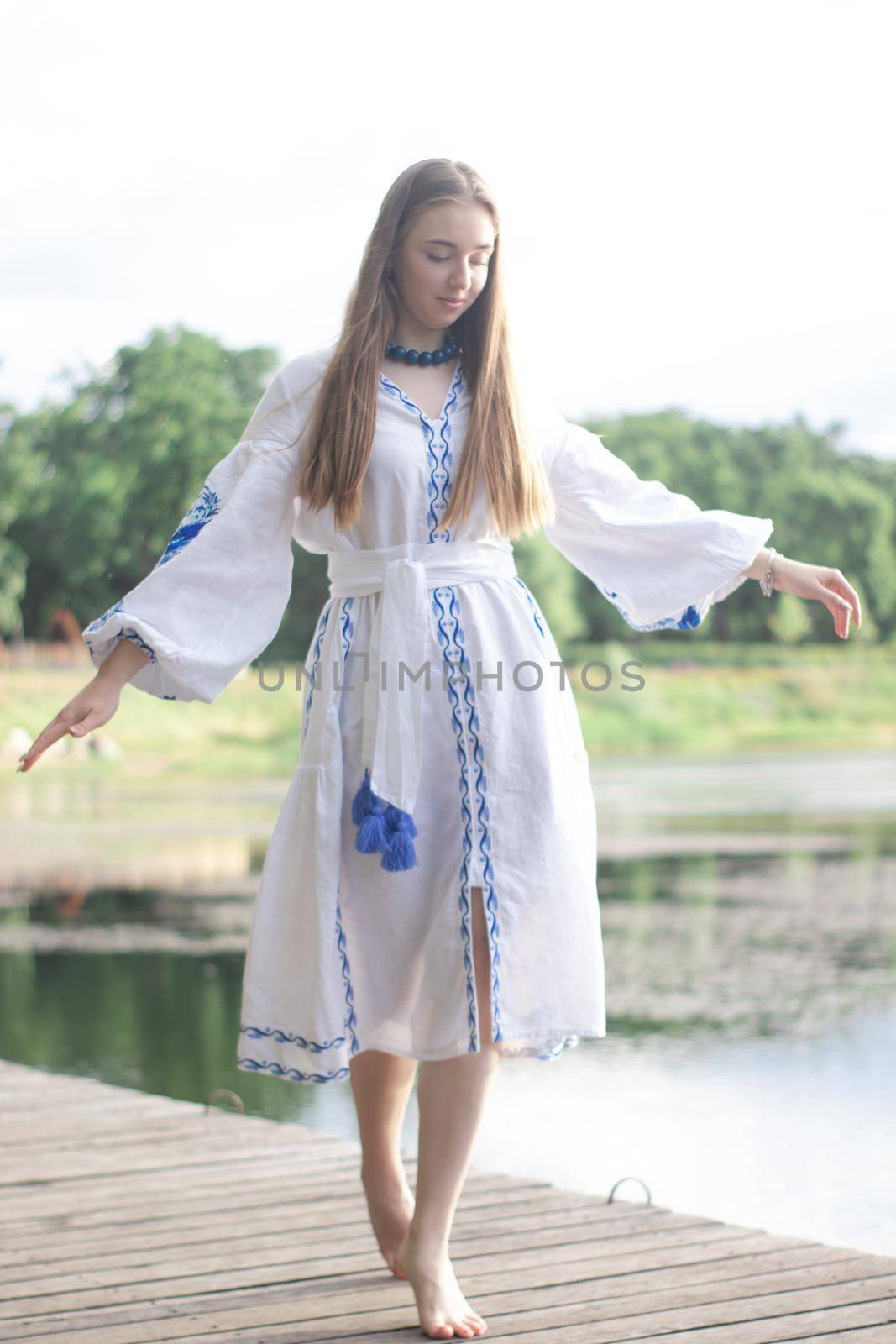 a girl in an embroidered Ukrainian shirt sits on the pier, the reflection of clouds in the water of the lake. On the shore of the sky. vyshyvanka day. freedom. patriot.