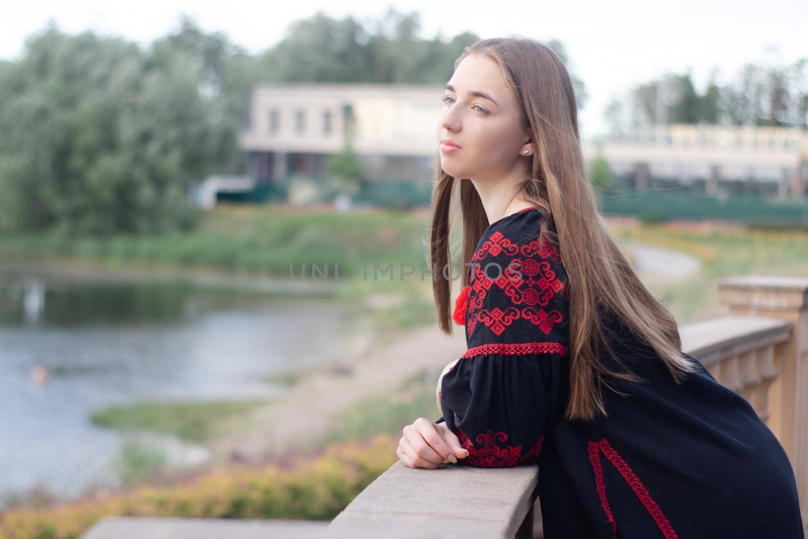 charming ukrainian young woman in embroidered national red and black dress outdoors. pretty girl in park wearing vyshyvanka.