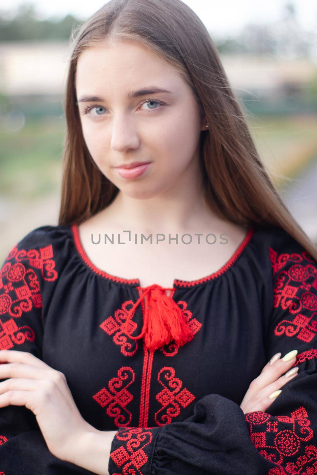 charming ukrainian young woman in embroidered national red and black dress outdoors. pretty girl in park wearing vyshyvanka.