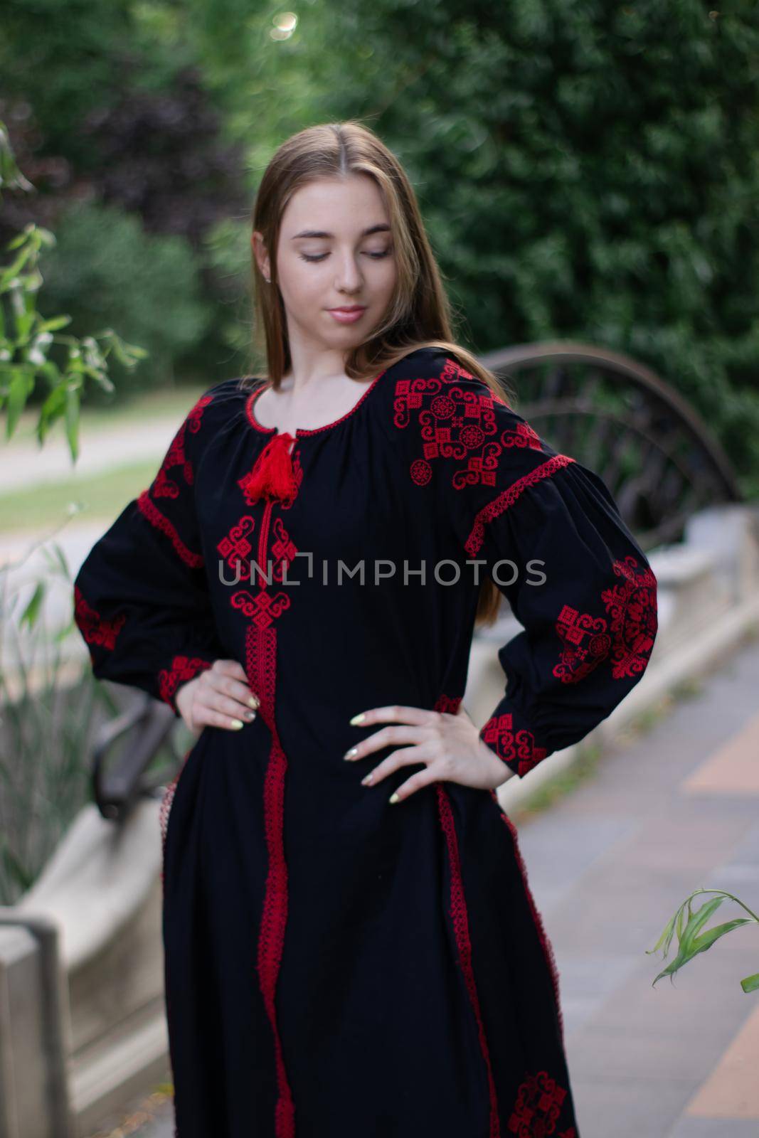 charming ukrainian young woman in embroidered national red and black dress outdoors. pretty girl in park wearing vyshyvanka.