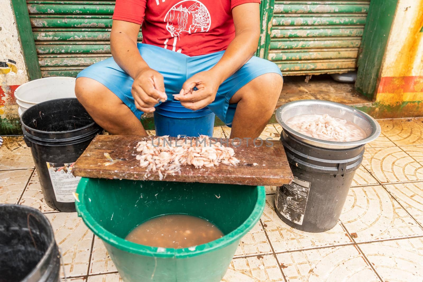 Unrecognizable man peeling shrimp in the street of a seafood market by cfalvarez