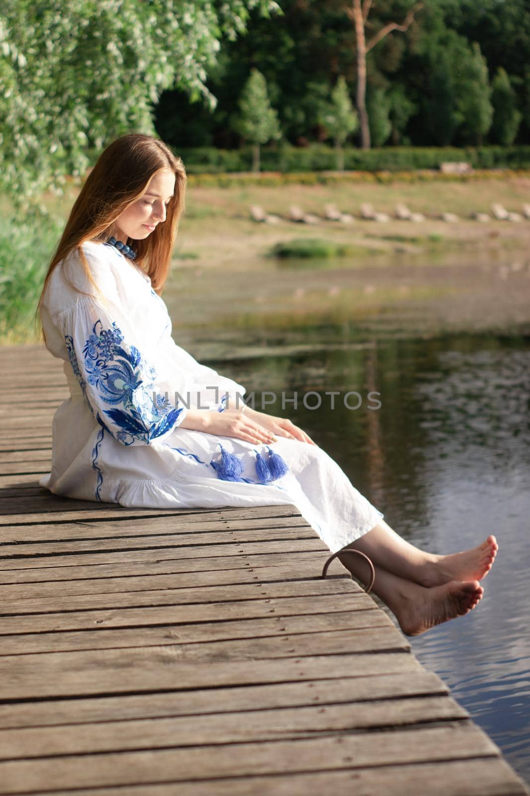 a girl in an embroidered Ukrainian shirt sits on the pier, the reflection of clouds in the water of the lake. On the shore of the sky. vyshyvanka day. freedom. patriot by oliavesna