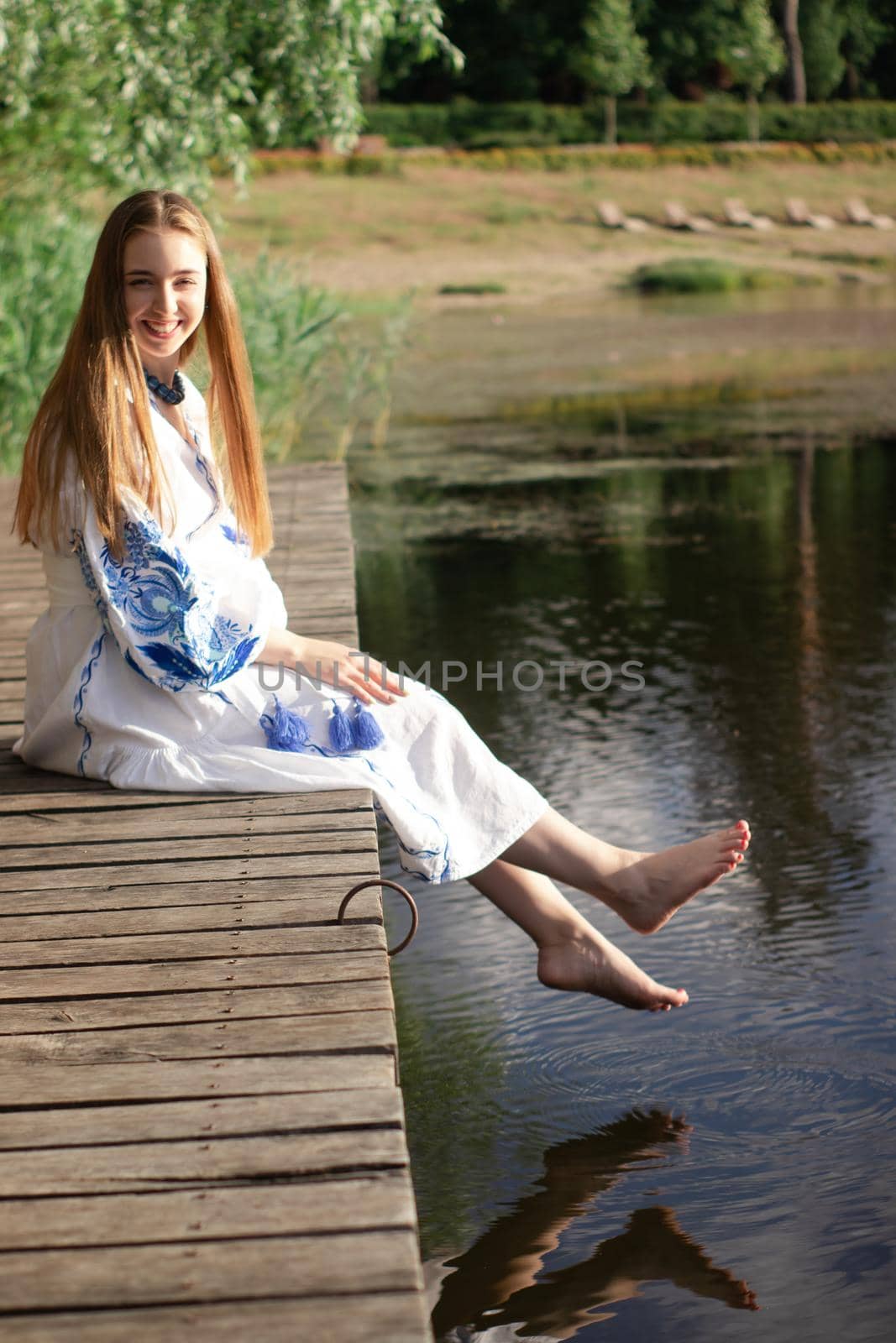 Girl in embroidered national Ukrainian costume on a pier on the shore of the lake. Independence day of ukraine, constitution, vyshyvanka day. young woman in blue dress outdoors.