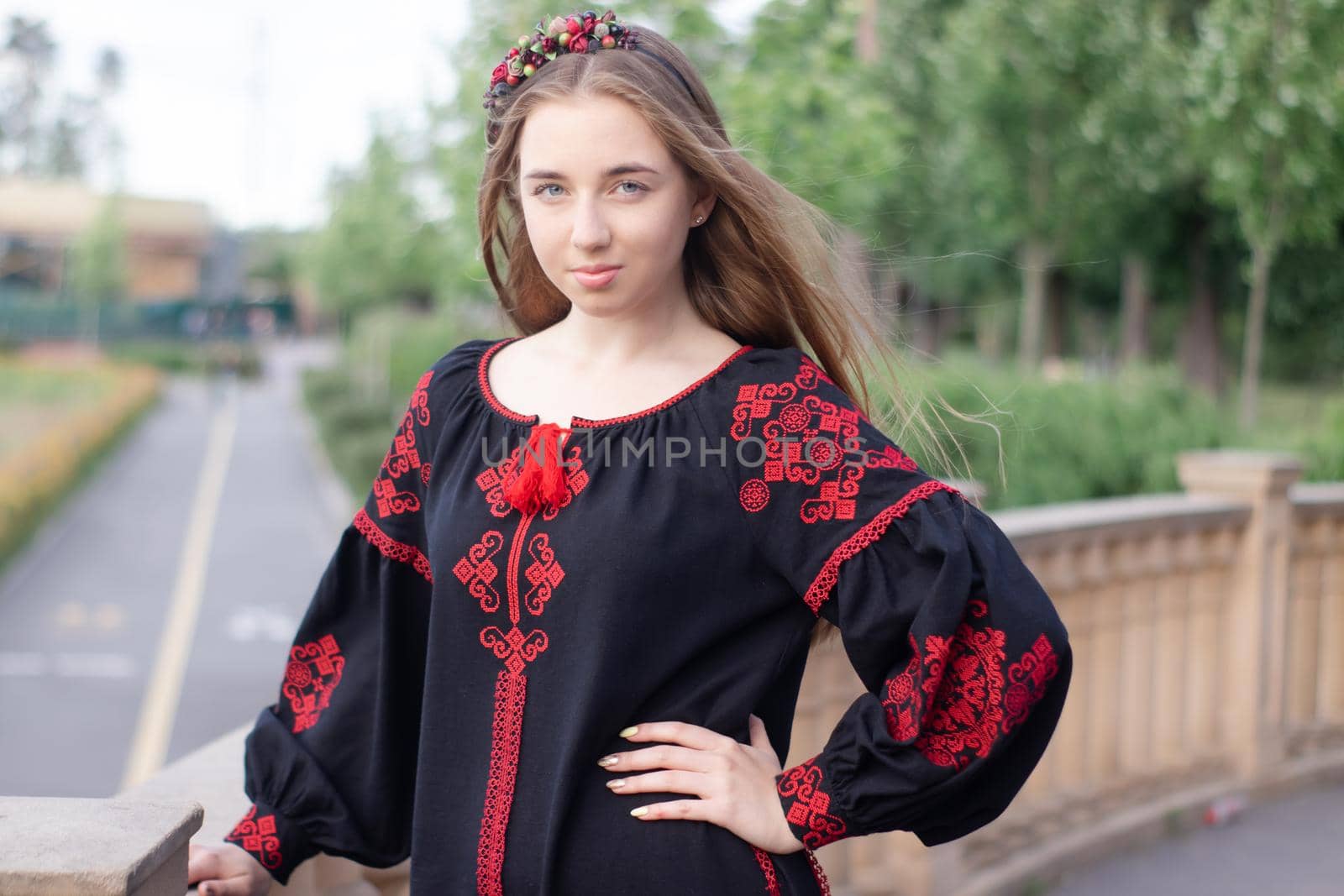 charming ukrainian young woman in embroidered national red and black dress outdoors. pretty girl in park wearing vyshyvanka by oliavesna