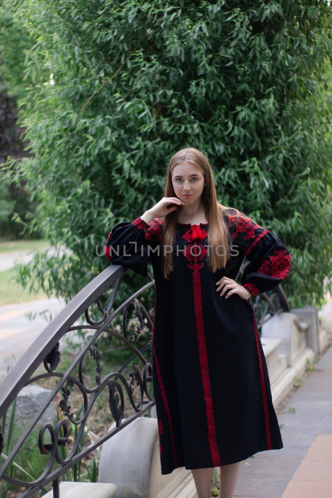 charming ukrainian young woman in embroidered national red and black dress outdoors. pretty girl in park wearing vyshyvanka.