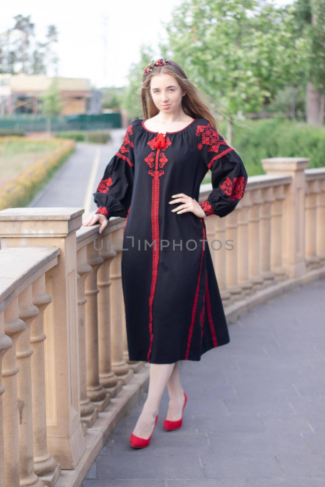 charming ukrainian young woman in embroidered national red and black dress outdoors. pretty girl in park wearing vyshyvanka by oliavesna