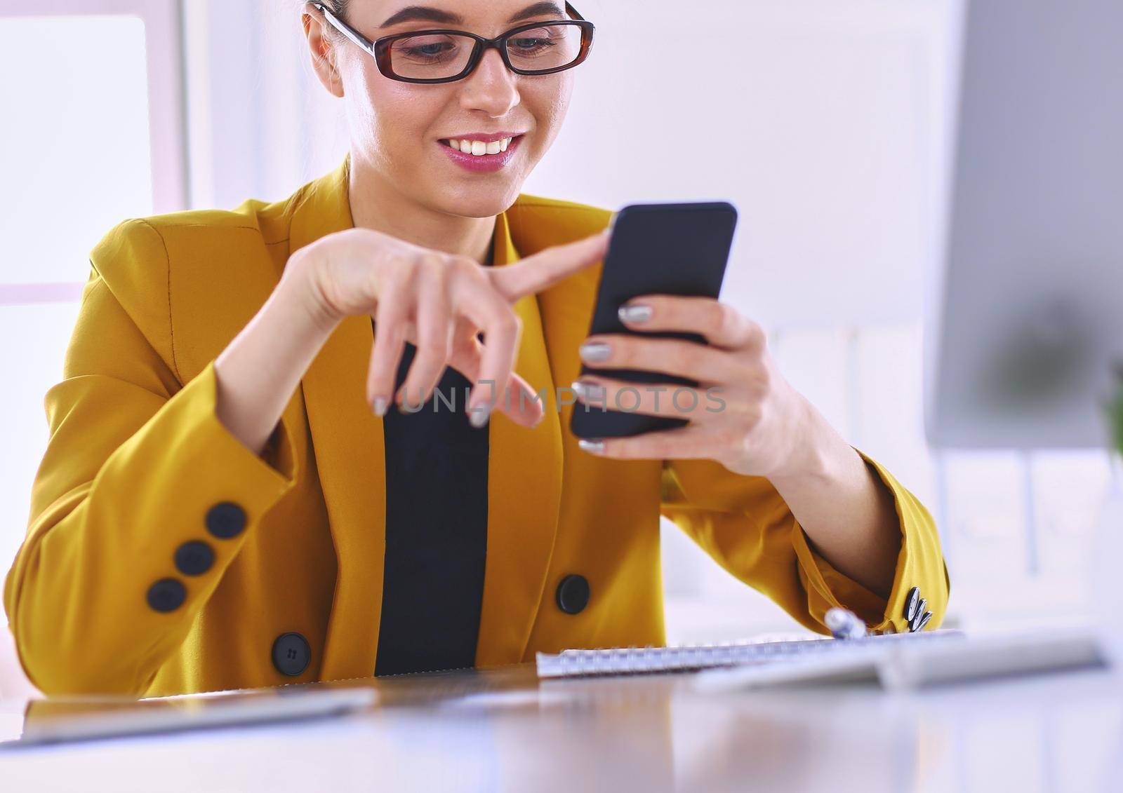 Portrait of businesswoman using mobile phone and text messaging while sitting at desk in front of laptop