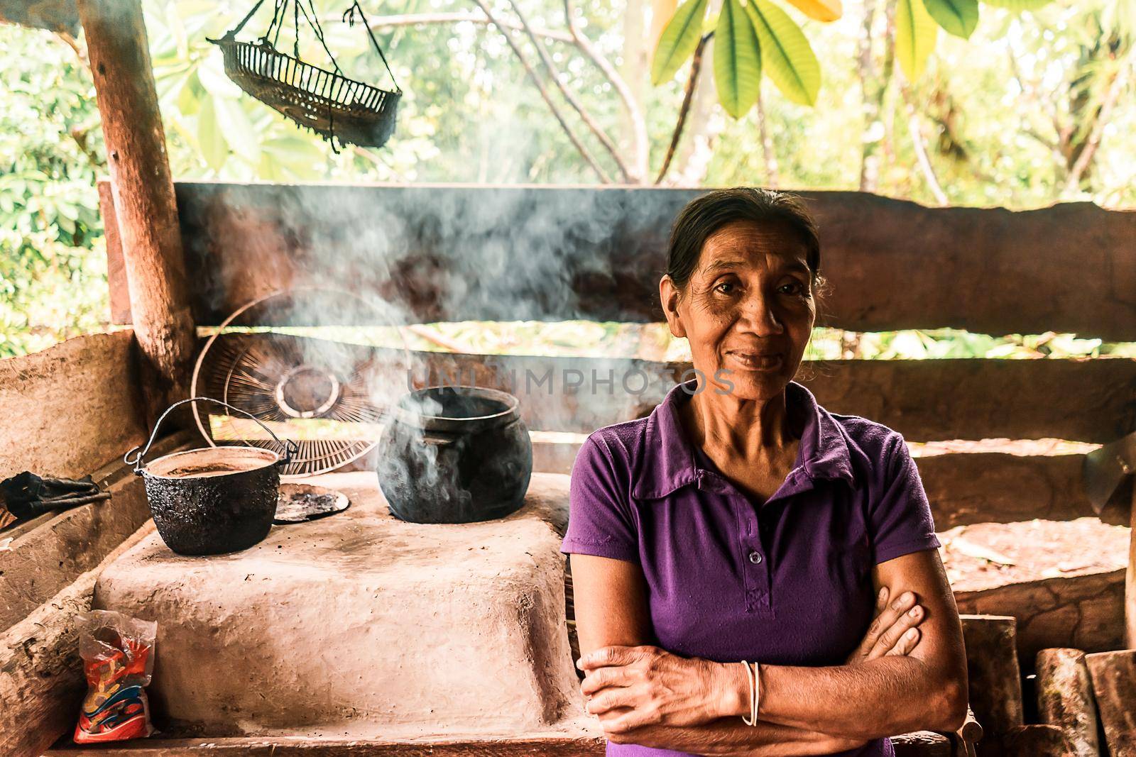 Latin grandmother with crossed arms smiling at camera in the kitchen of her house by cfalvarez