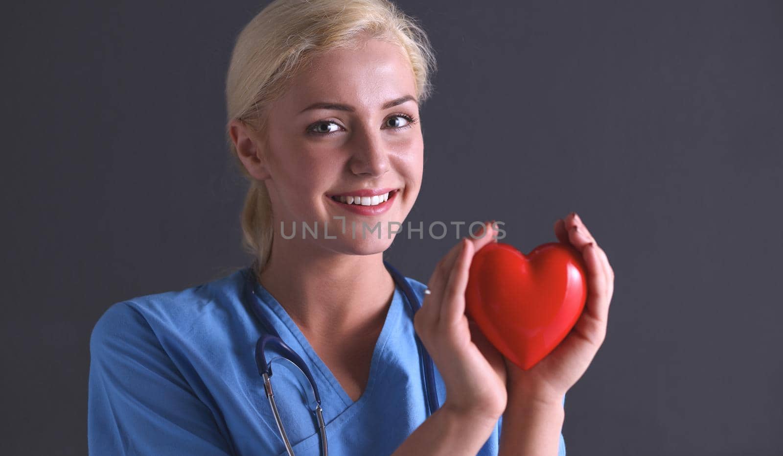 Female doctor with stethoscope holding heart, isolated on grey background