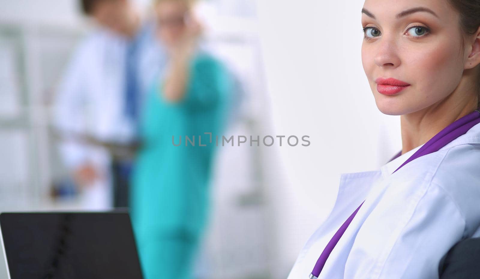 Beautiful young smiling female doctor sitting at the desk.