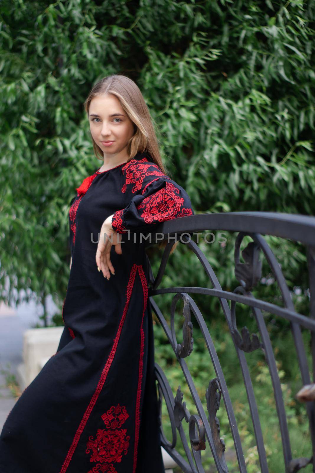 charming ukrainian young woman in embroidered national red and black dress outdoors. pretty girl in park wearing vyshyvanka by oliavesna