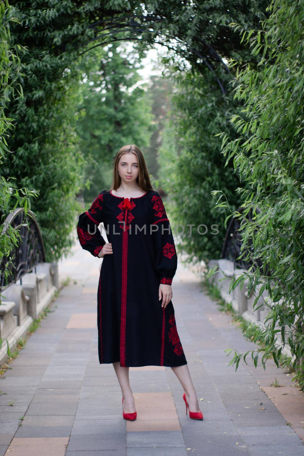 charming ukrainian young woman in embroidered national red and black dress outdoors. pretty girl in park wearing vyshyvanka.