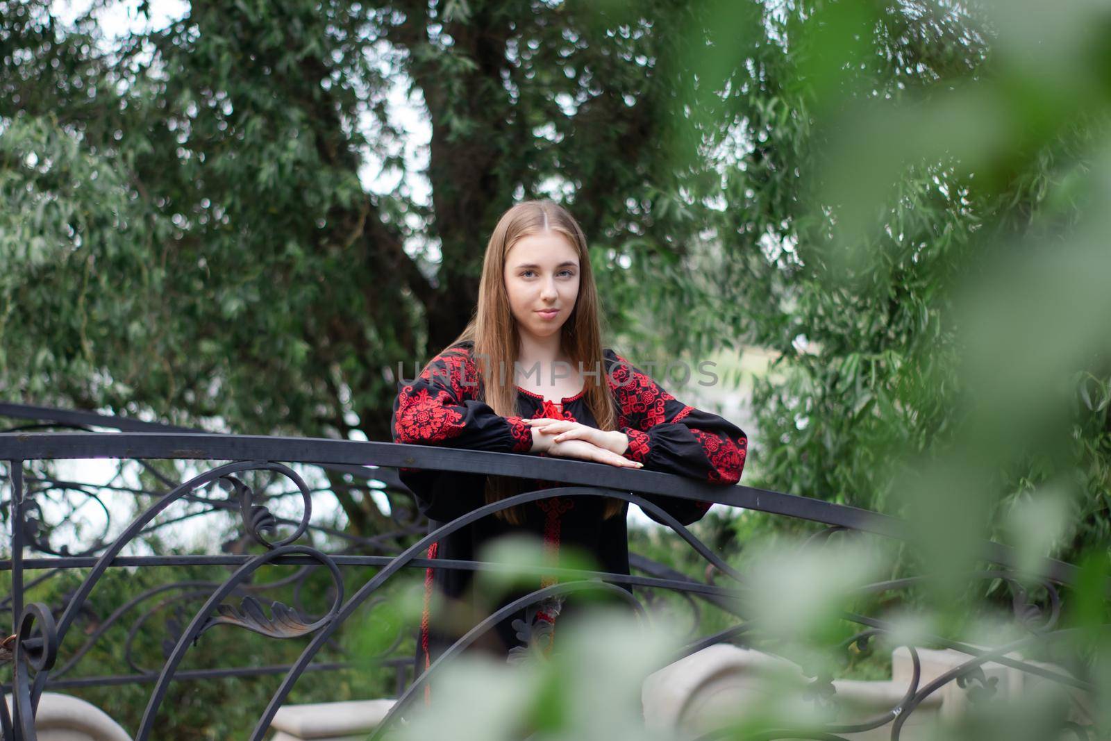 charming ukrainian young woman in embroidered national red and black dress outdoors. pretty girl in park wearing vyshyvanka.
