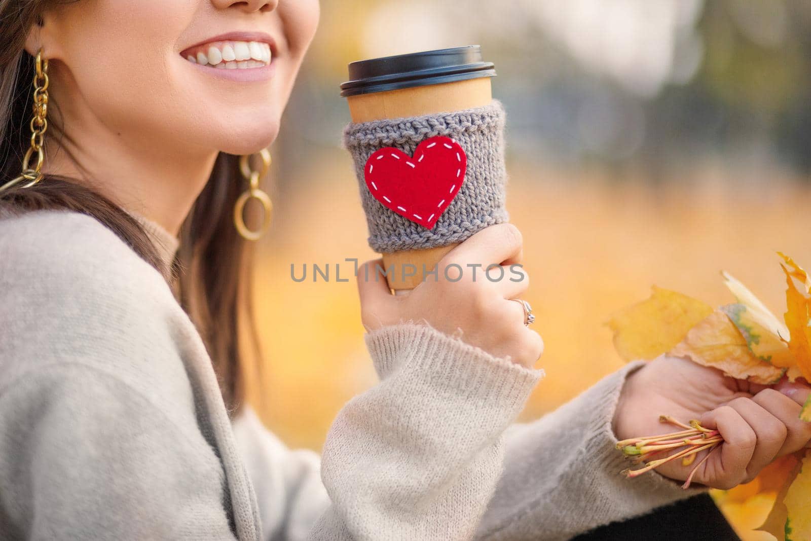 Paper cup with coffee in woman's hands in autumn park.