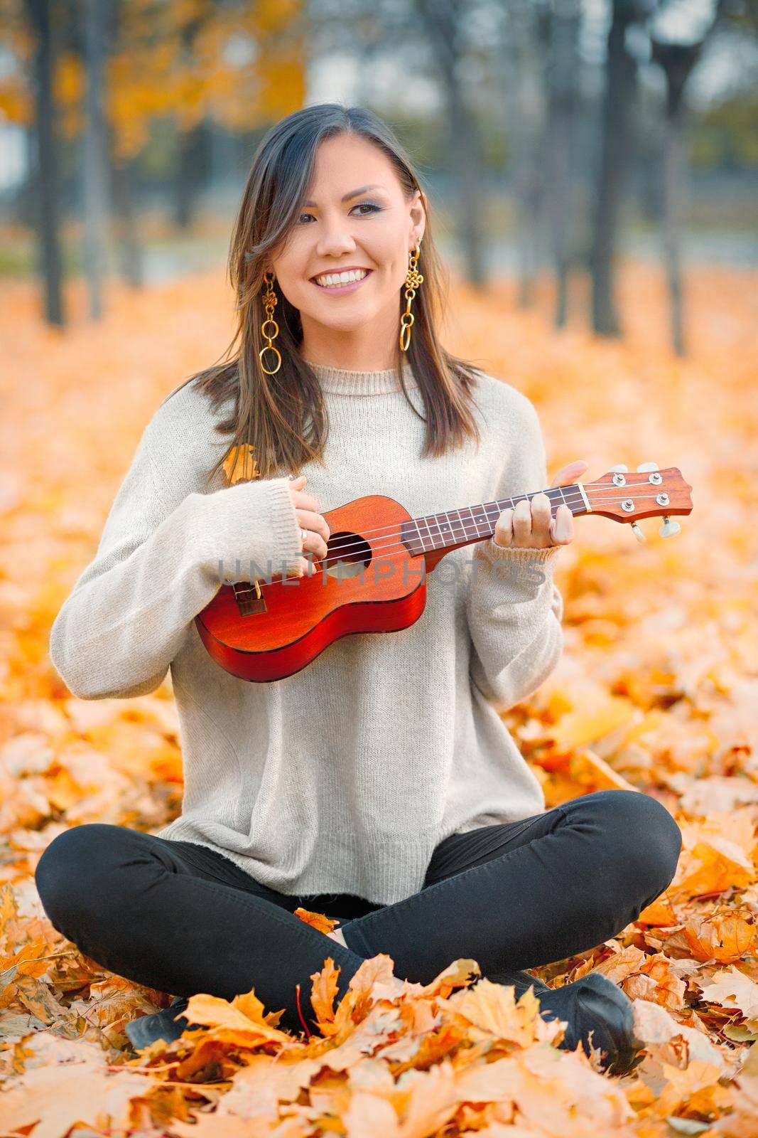 Young beautiful mixed race woman playing ukulele and smiling in autumn park.