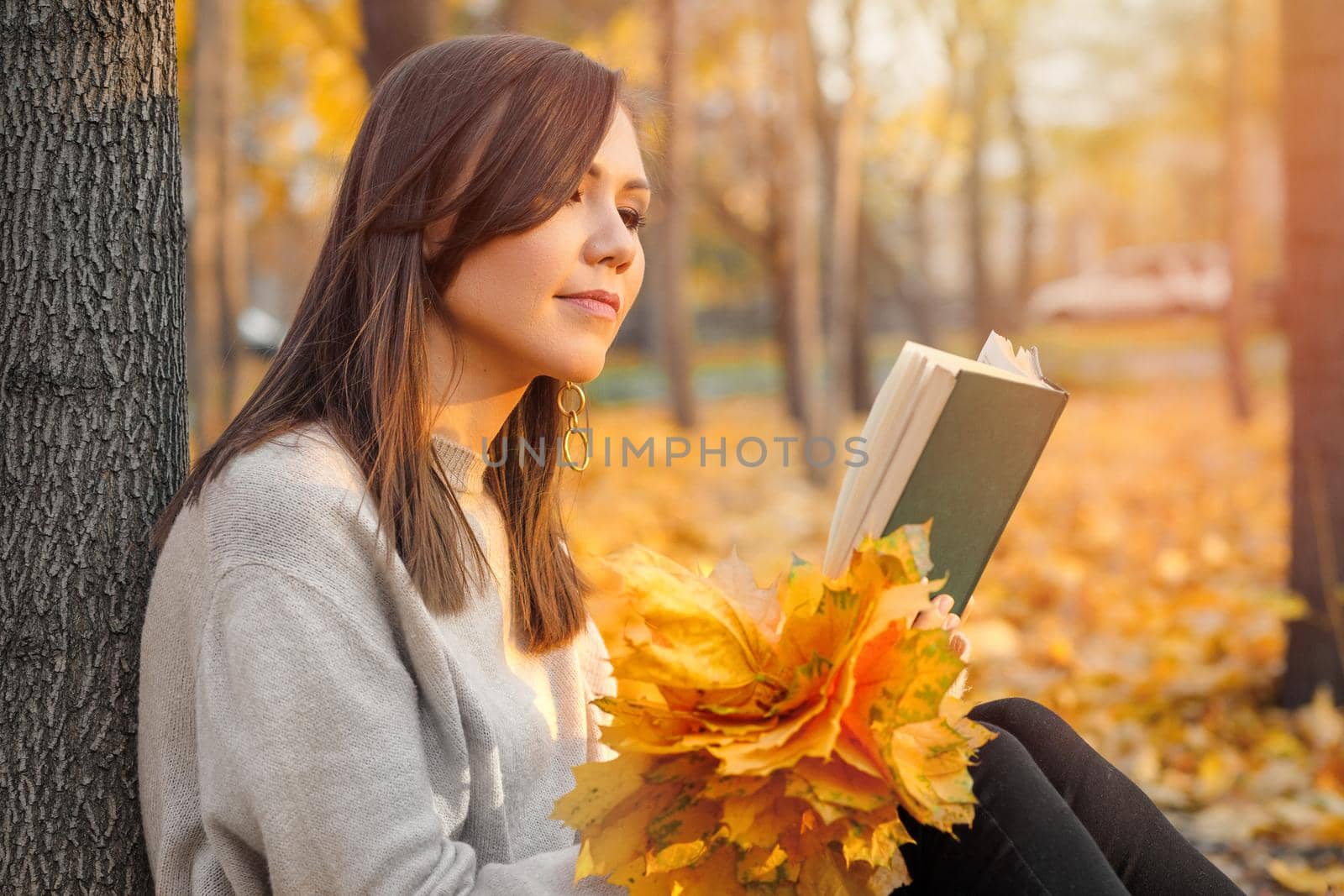 A young woman reads a book near a tree in an autumn park. The concept of self-development.