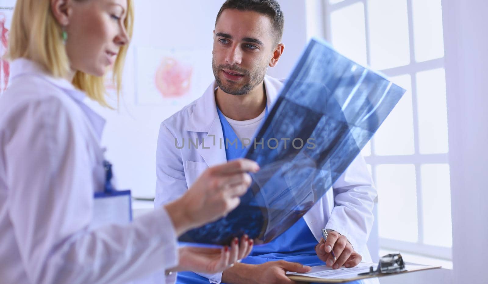Handsome doctor is talking with young female doctor and making notes while sitting in his office