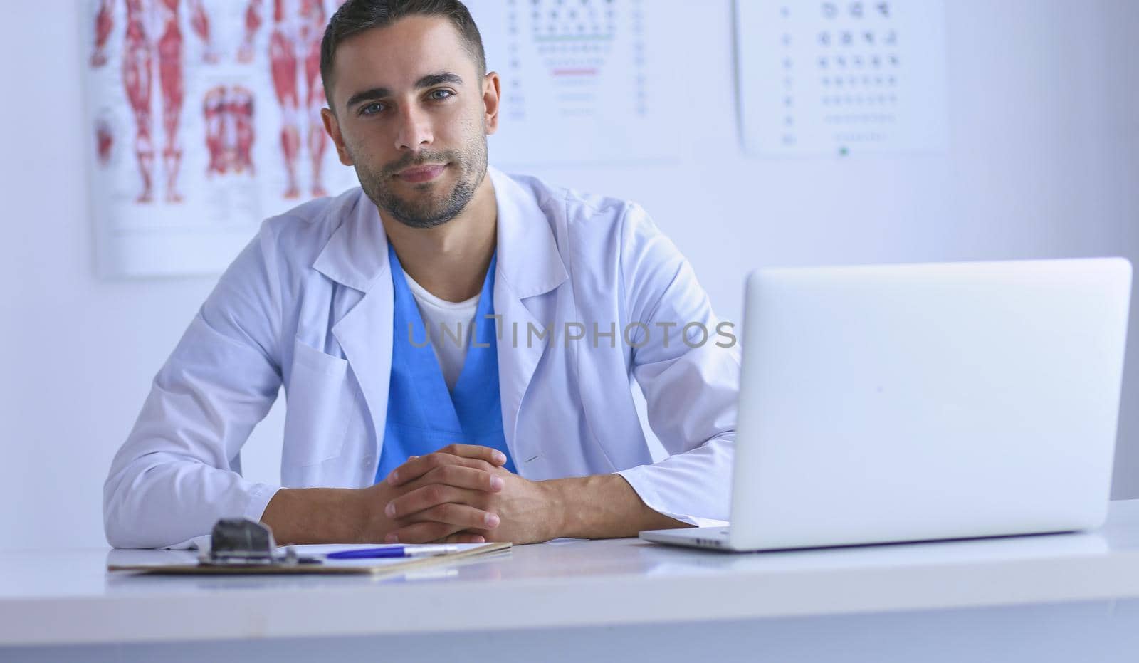 Portrait of a male doctor with laptop sitting at desk in medical office