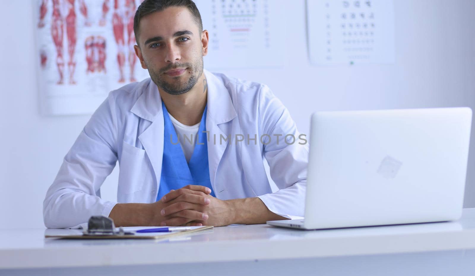 Portrait of a male doctor with laptop sitting at desk in medical office