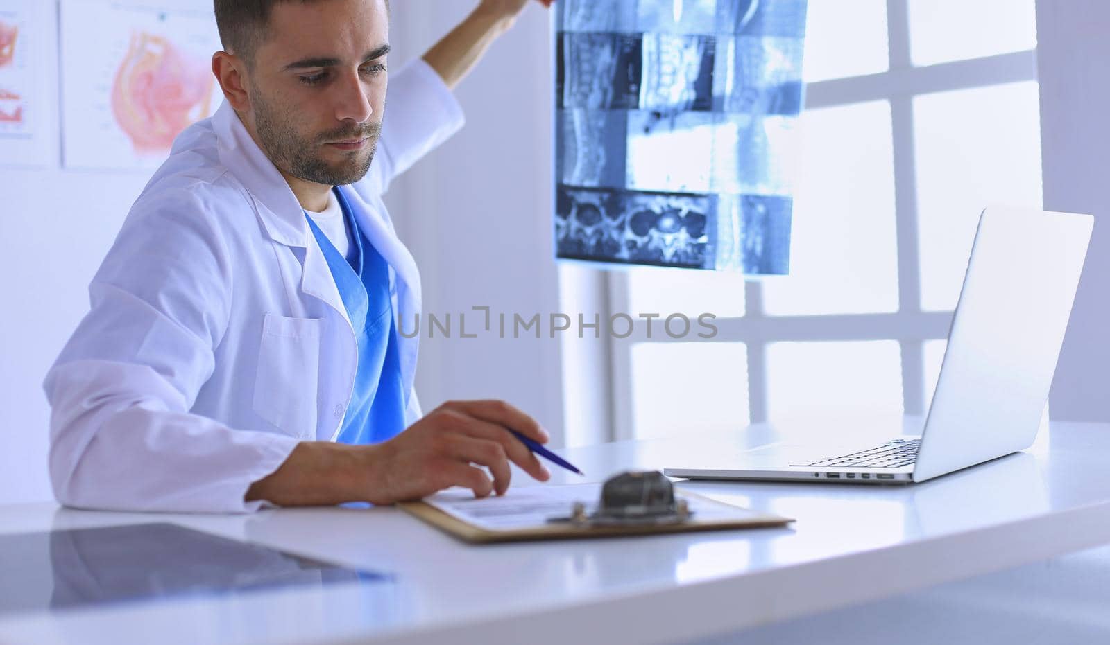 Handsome doctor is talking with young female patient and making notes while sitting in his office