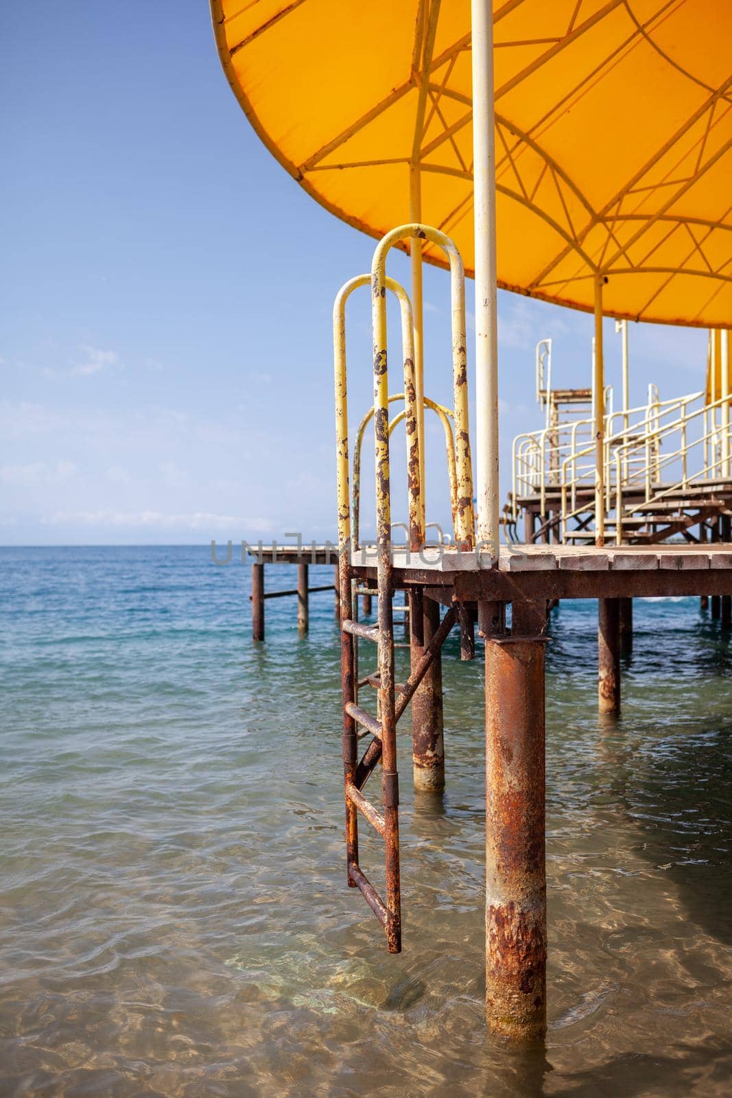 Swimming area or pier on the sea. A large pier with a roof, wooden planks and rusty stairs descending into the water. Bathing and resting place.