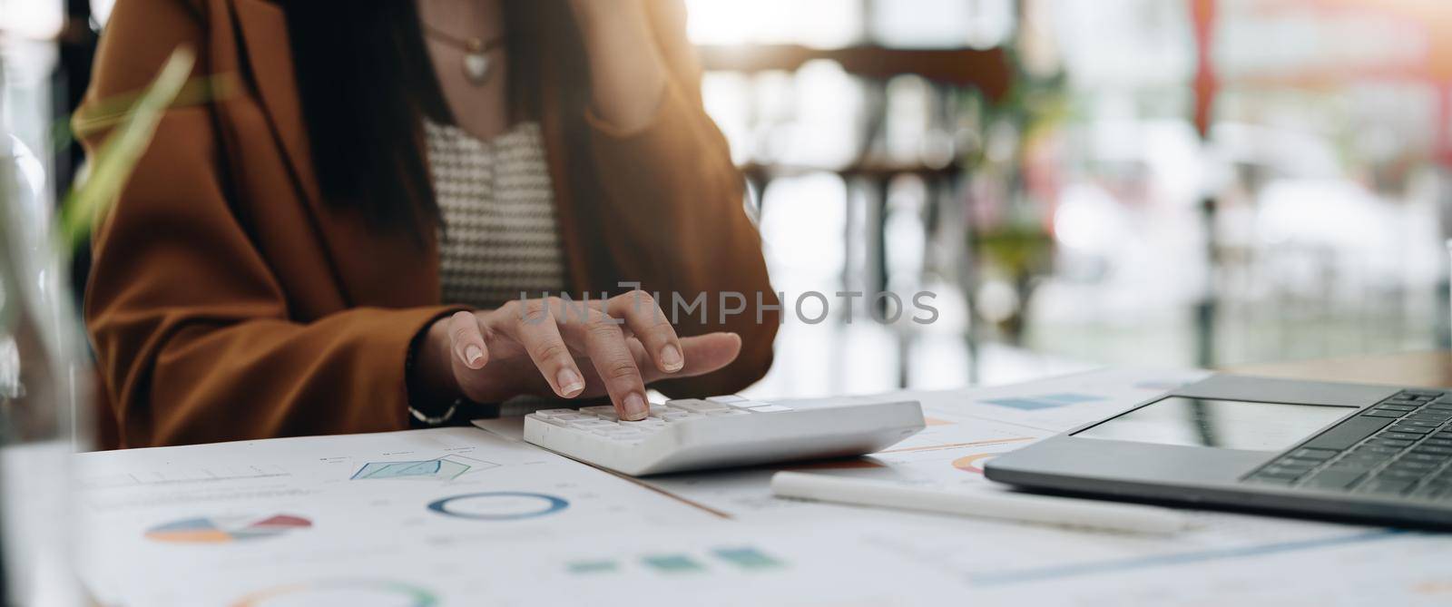 Close up of businesswoman or accountant working on calculator to calculate business data, accountancy document and laptop computer at office, business concept by nateemee