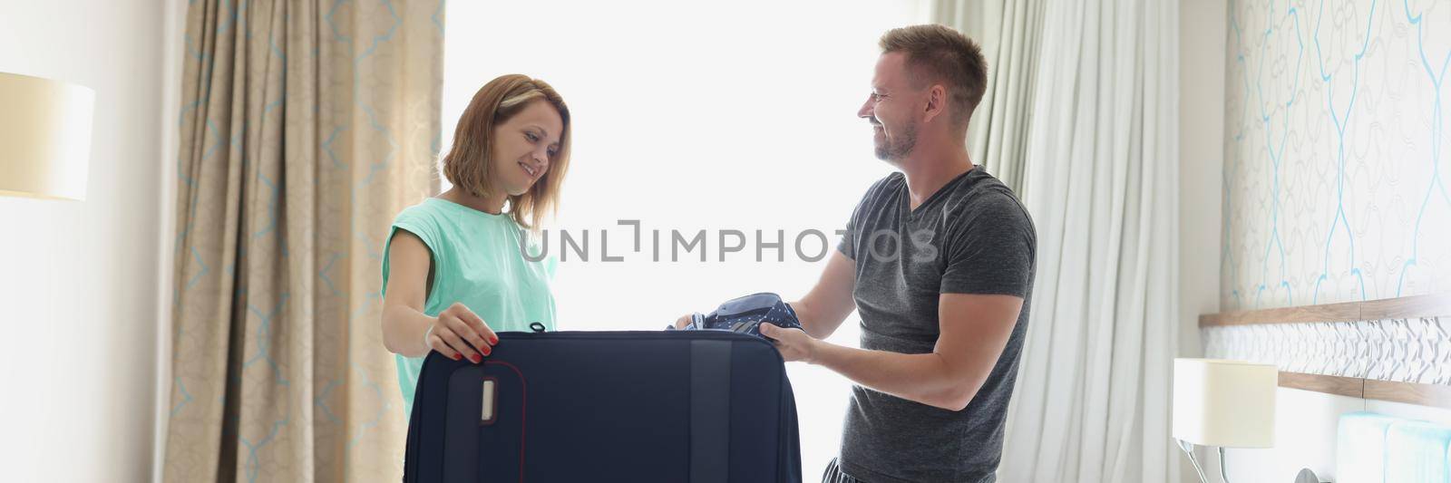 Portrait of woman wife help husband to pack stuff in suitcase for work trip. Woman smile and give advice to man. Work trip, farewell, family time concept