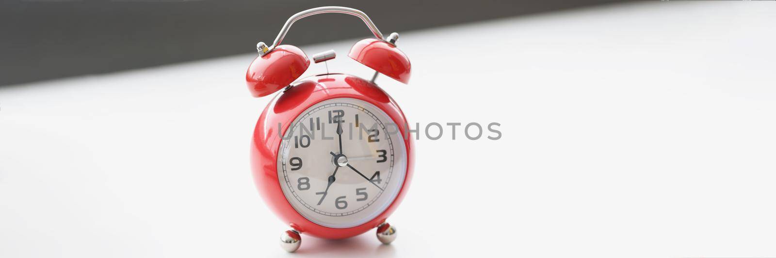 Close-up of retro red clock on white surface show seven in morning, wakeup, time for work. Set alarm for specific time. Vintage, time, late, design concept