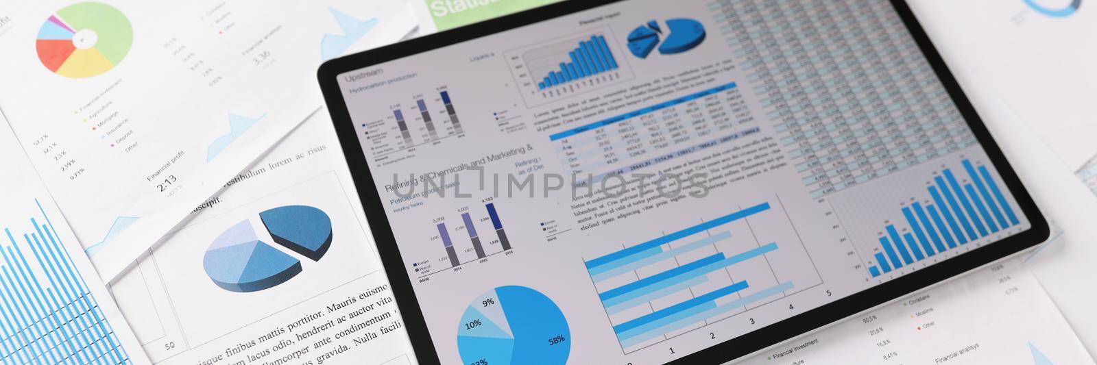 Close-up of workplace mess filled with business papers, tablet with diagrams and charts on device screen. Business, strategy, statistics, report concept