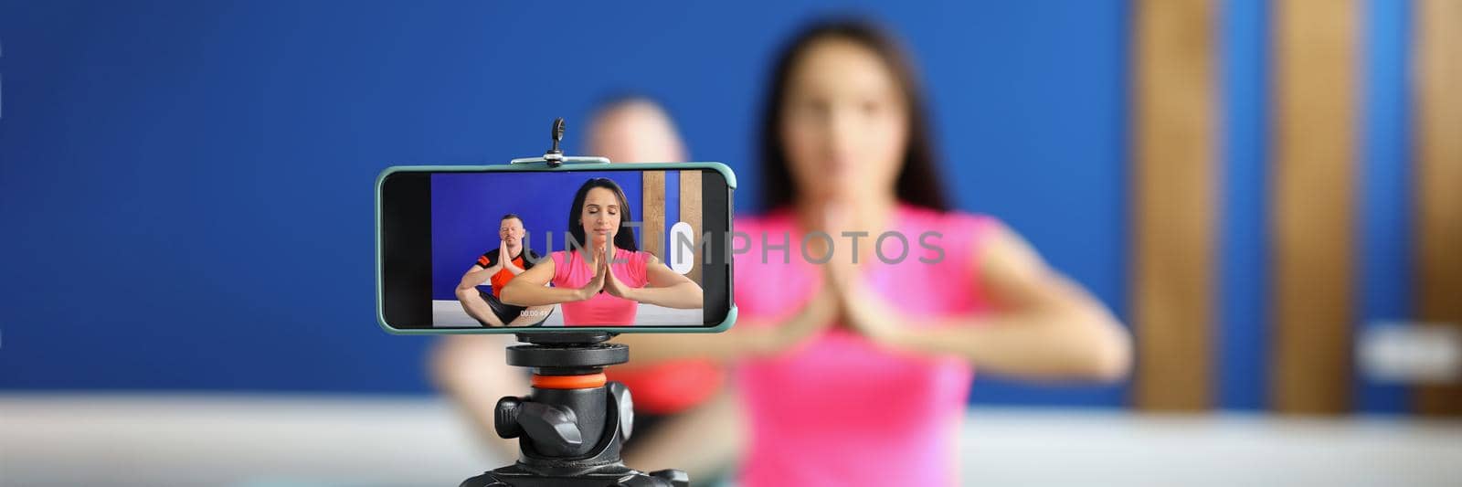 Camera on tripod filming people perform asana on mat in studio by kuprevich