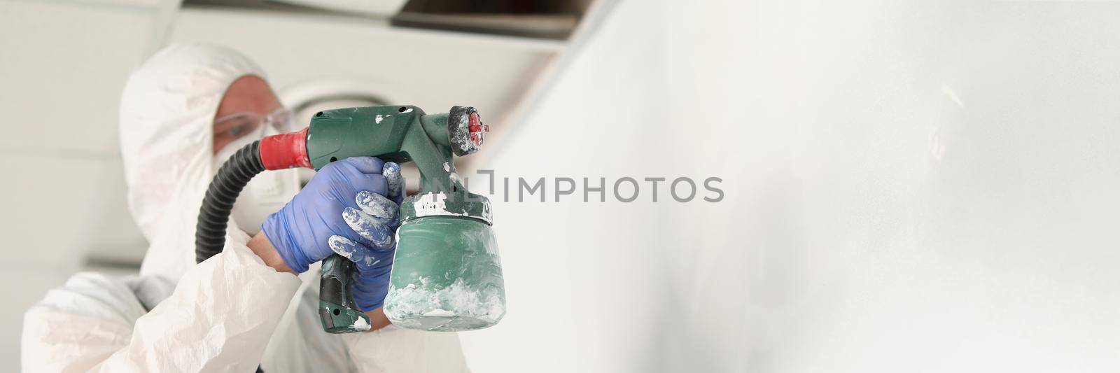 Close-up of male worker painting wall with spray gun in white colour, busy handyman at work. Renovation, construction site, interior, household concept
