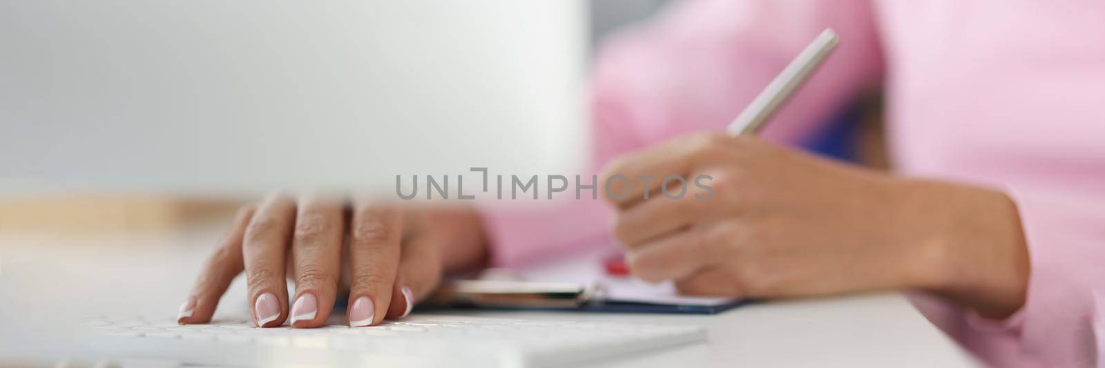 Close-up of person writing down ideas in journal on working place, making notes for future, planning day. Typing on keyboard at same time. Planner concept