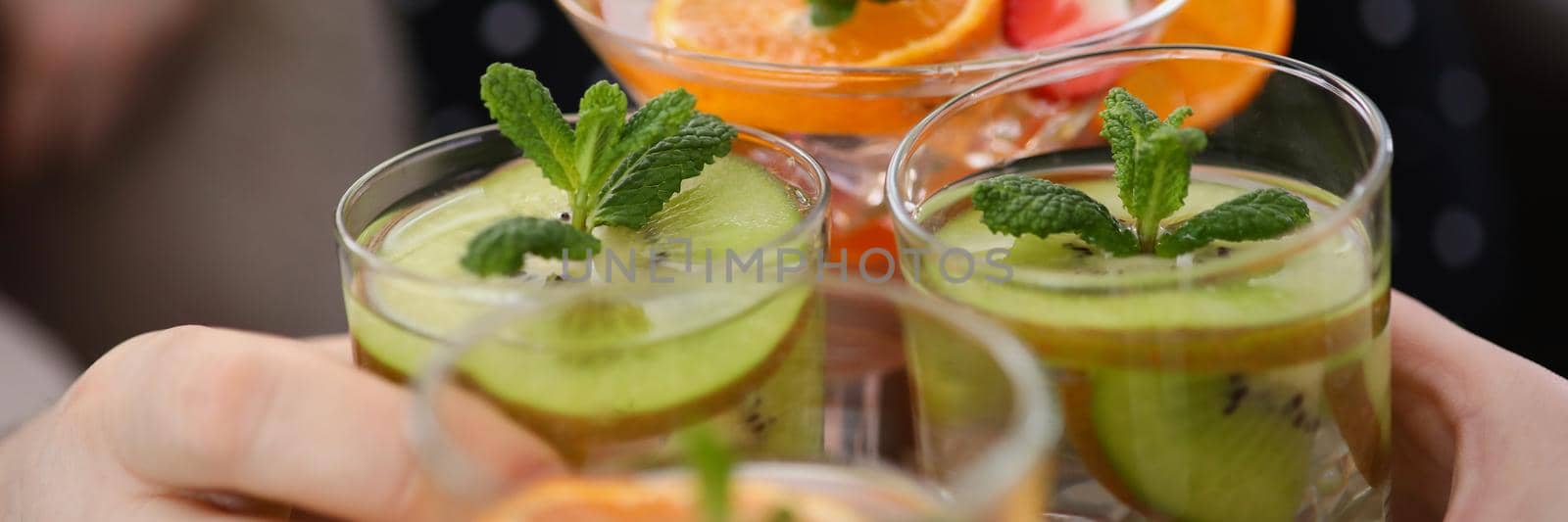 Close-up of group of people with cooling drinks make clink with glasses, raise toast. Summer fruit beverages, tasty alcoholic drinks. Party, fun concept